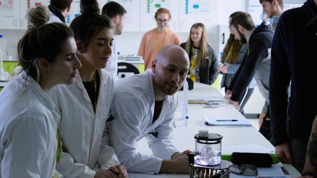 A group of people in lab coats gathered around lab table
